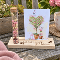 Houten fotoplankje met glazen buisje gevuld met roze en witte droogbloemen en een kaart met een hartvormige boom.
