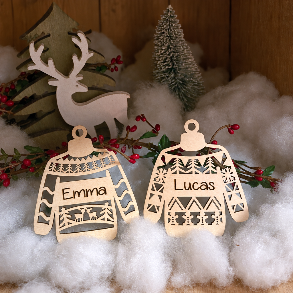 Twee houten kerstballen in de vorm van truitjes met gegraveerde namen Emma en Lucas en winters motief.
