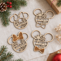 Vier houten kerstballen in de vorm van Minnie en Mickey Mouse met gepersonaliseerde namen en sneeuwvlokken op een stoffen ondergrond.